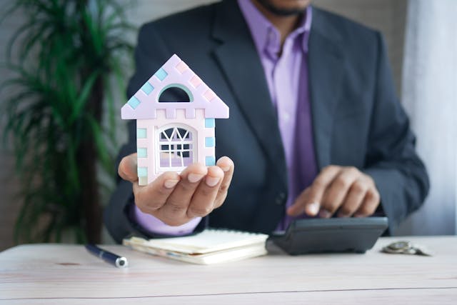 a-person-holding-a-home-figurine-and-putting-numbers-into-a-calculator