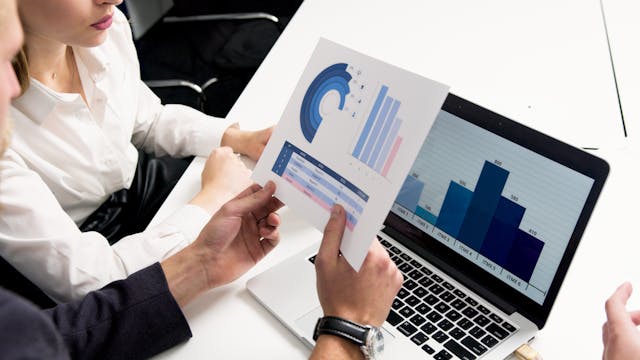 A man and a woman, mostly cropped, looking at charts on a piece of paper and a computer.